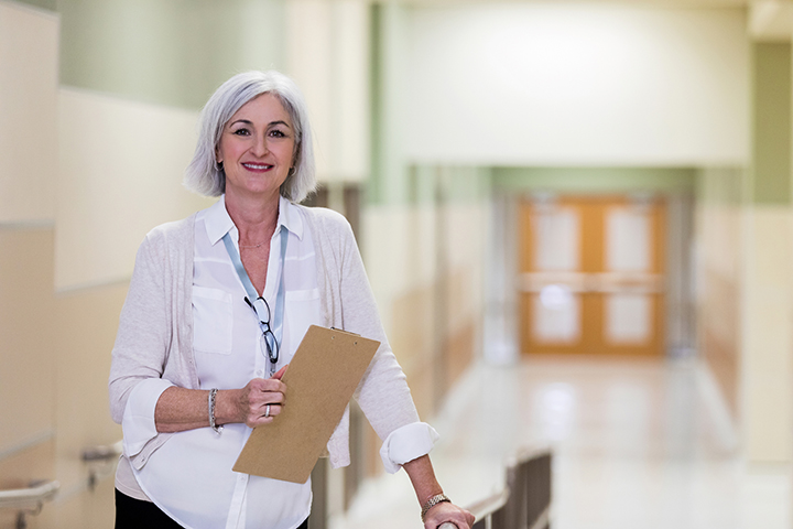 Administrator or staff person standing in school hallway holding a clipboard