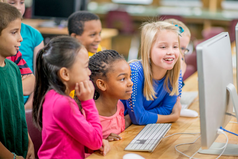 Multiple elementary students looking at a desktop computer monitor